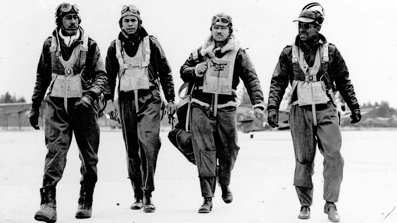 4 WWII-era African American men in flight suits walk toward the camera