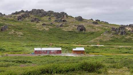 A red cabin surrounded by greenery and knolls.