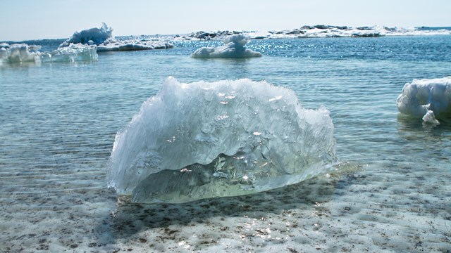A chunk of clear ice floats in crystal clear water with more sea ice in the background.