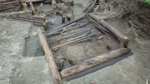 From above, several archaeologist work on the excavation of a semi-subterranean driftwood house. 