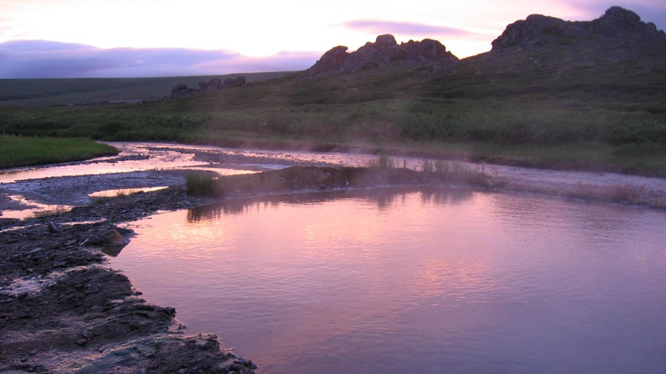 A dusky sky is reflected upon a shallow pool surrounded by jagged rock. 