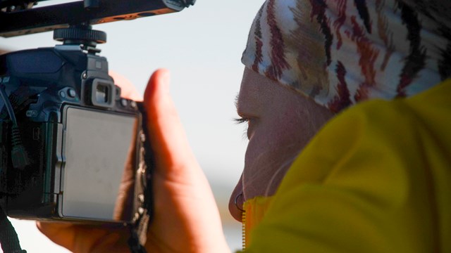 A woman looks closely at her DSLR camera. 