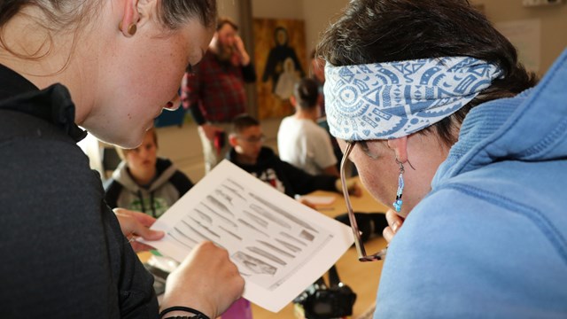 Two woman look at a diagram depicting several Inupiat tools. 