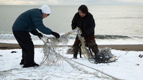 Two people untangle a net on the beach. 