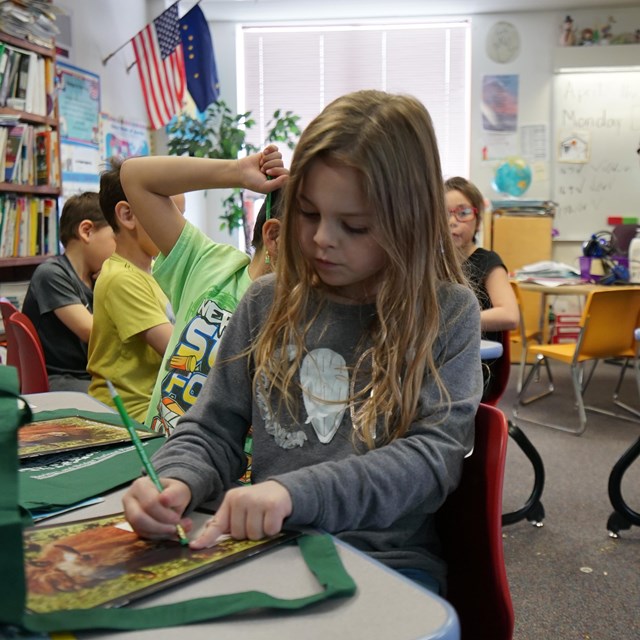 A girl working on her Junior Ranger book while a park ranger teaches.