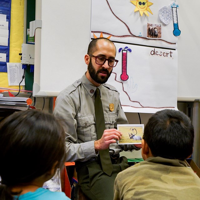 A park ranger holding an image of a caribou while speaking to a group of students.