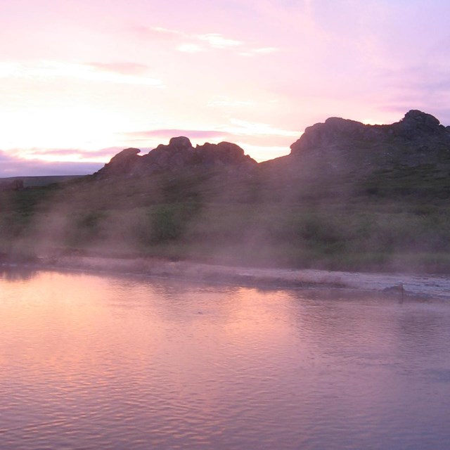 A small pool of water reflects a dusky sunset. 