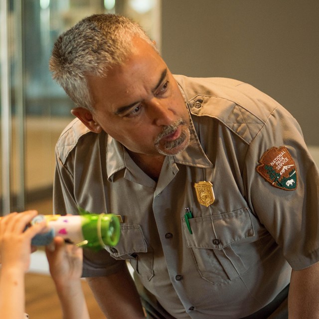 A park ranger helps a student look through a telescope.