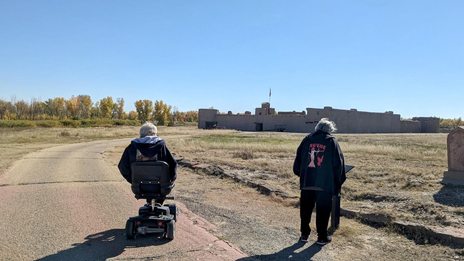 One visitor in motorized wheelchair is accompanied by another visitor reading signage