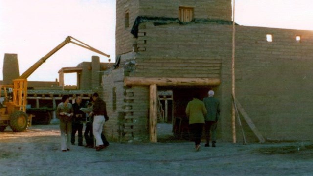 A photograph showing heavy equipment in an adobe fort with a wall missing. 