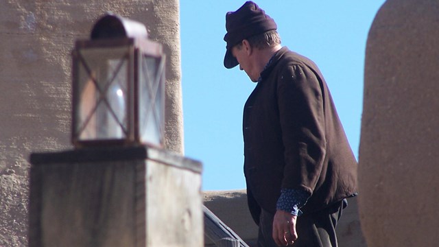 A man in historic costume walks along the second level of the fort. 