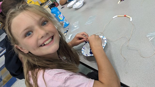 Girl smiles while making a beaded necklace