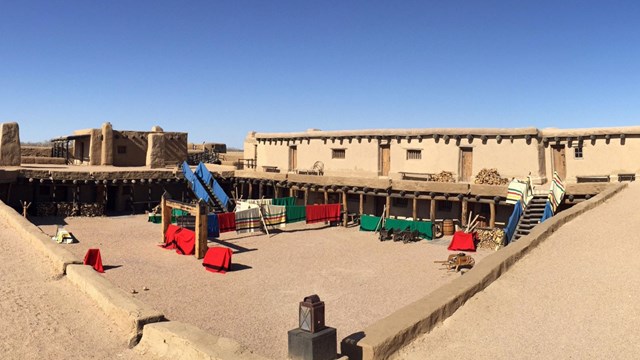 The interior of an adobe for showing a rectangular plaz on the ground floor with blankets displayed.