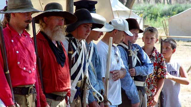 Costumed volunteers and visitors stand in a line carrying replica firearms. 