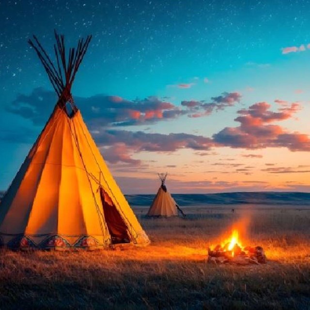 Four Southern Plains tipis against the night sky with a lit campfire