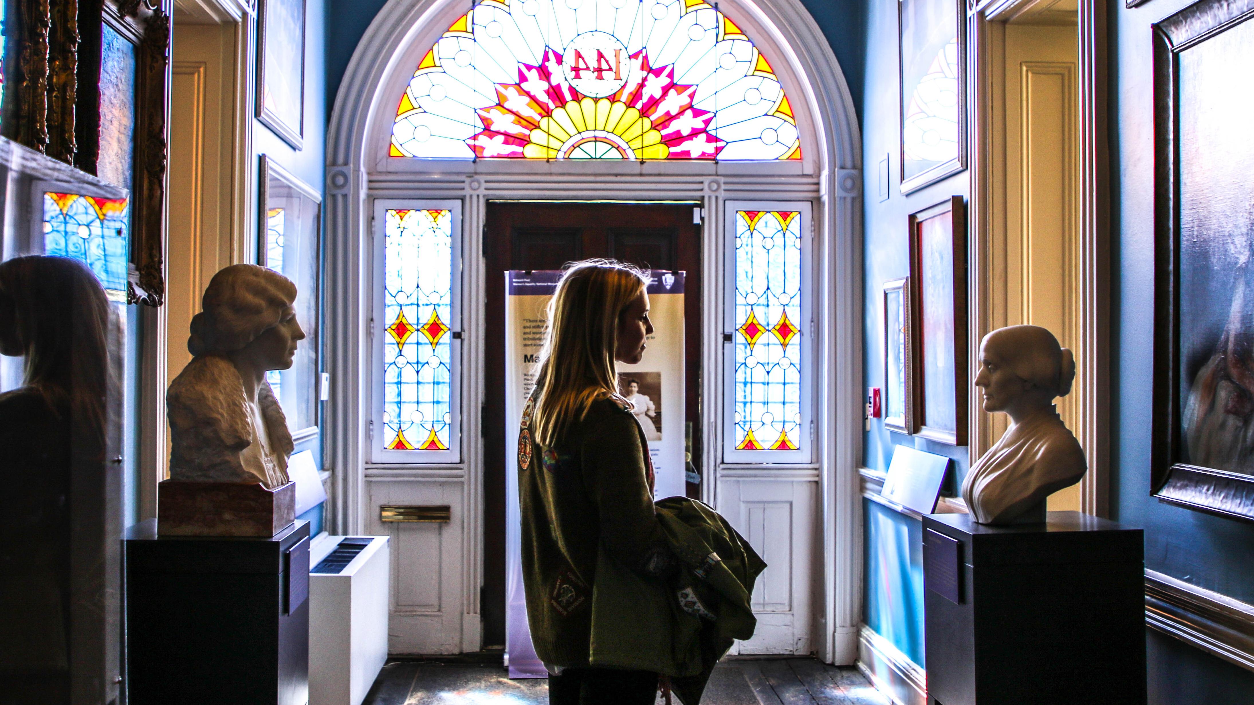 Woman in the hallway of the Belmont-Paul museum filled with pictures and statues