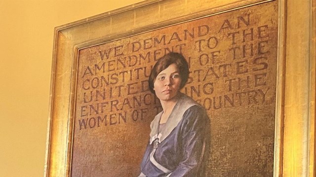 Park Ranger smiles next to painting on mantle of young Alice Paul