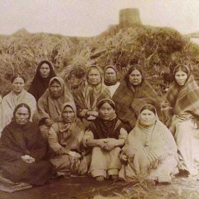 Group of women infront of semisubterranian dwelling