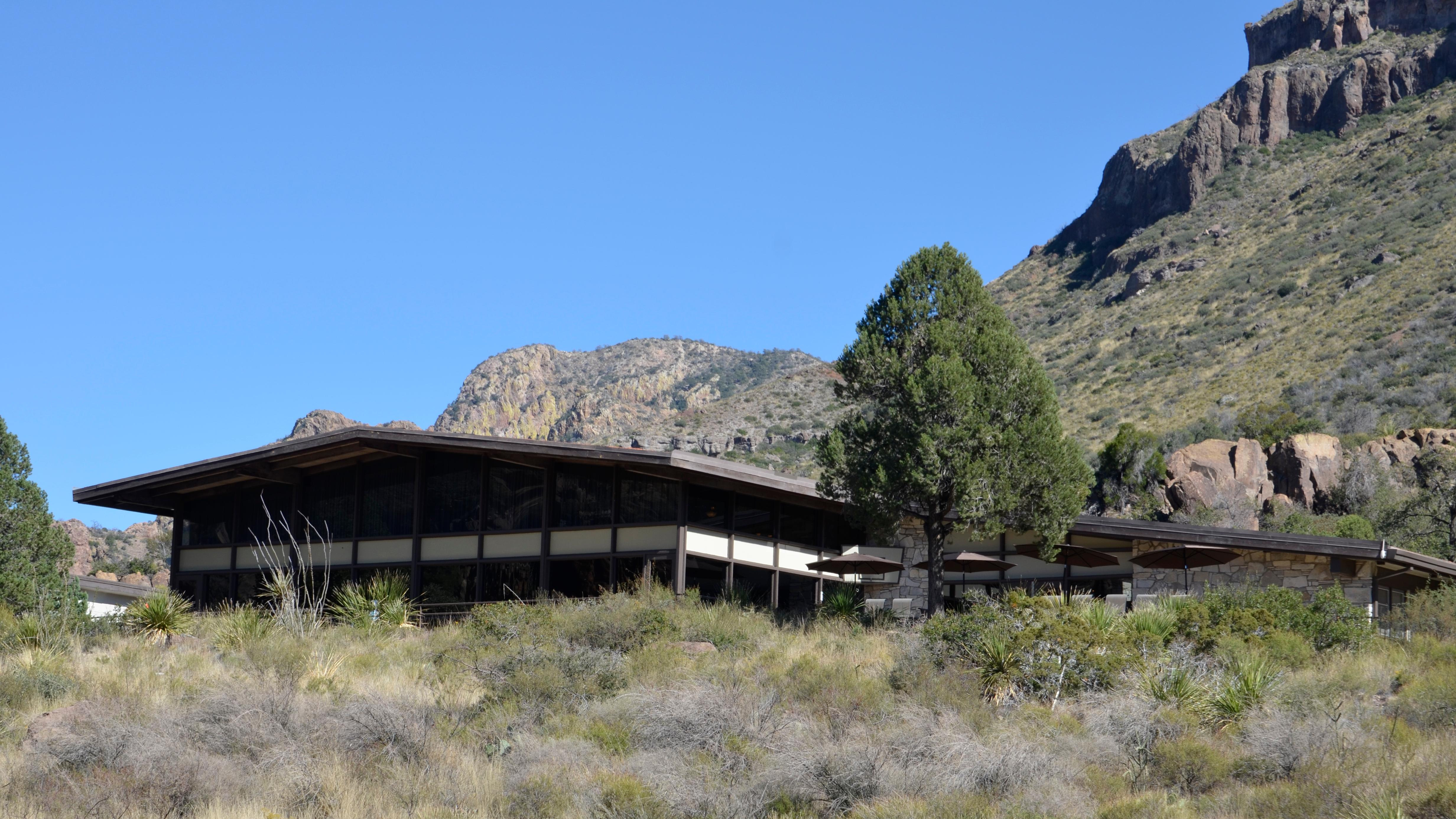 A large structure sits at the base of a mountain, surrounded by trees and grass.