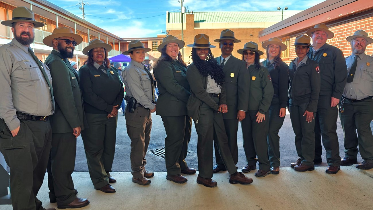 A group of rangers stand in a line. A two-story brick building is behind them.