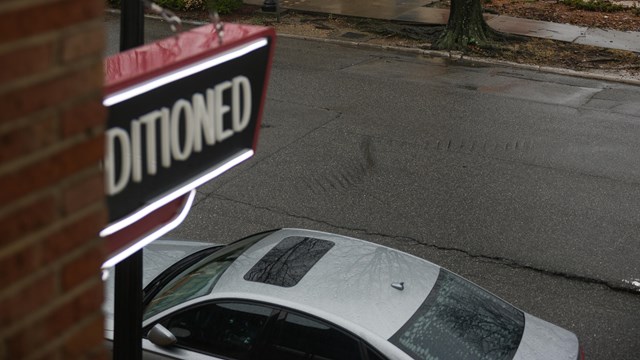 A road with streetlights. Parked on the road is a 4 door car. Part of a sign is visible.