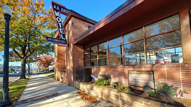 A brick building is dappled with late afternoon light. The sign says A.G. Gaston Motel.