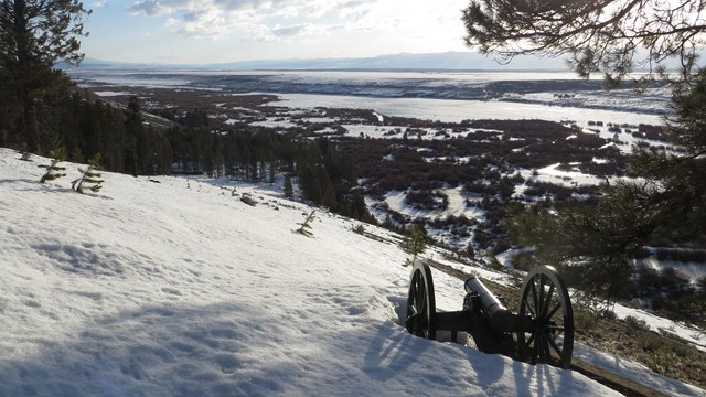 A mountain howitzer cannon sits on a snowy hillside overlooking a wintry valley.