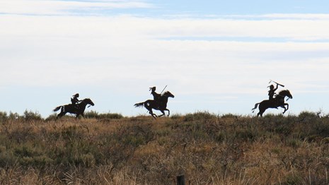 Three silhouette statues of Nez Perce on horseback in the distance.