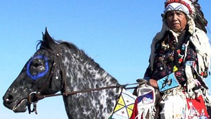 Nez Perce man in full regalia riding an apaloosa horse.