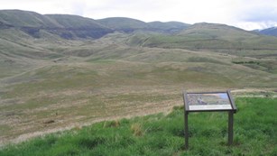 Vista of rolling hills and canyons with an information panel about the battle in the foreground.