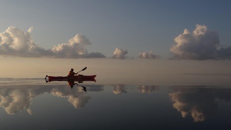 Silhouette of a person in a kayak paddling across glassy waters 