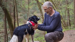 A visitor pets his dog on a trail