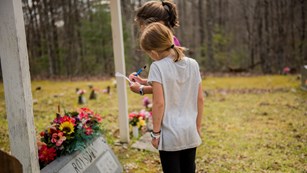 Two young girls look at a grave stone