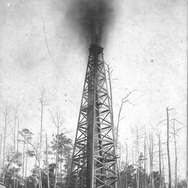 historic black and white photo of gushing oil derrick and nearby workers