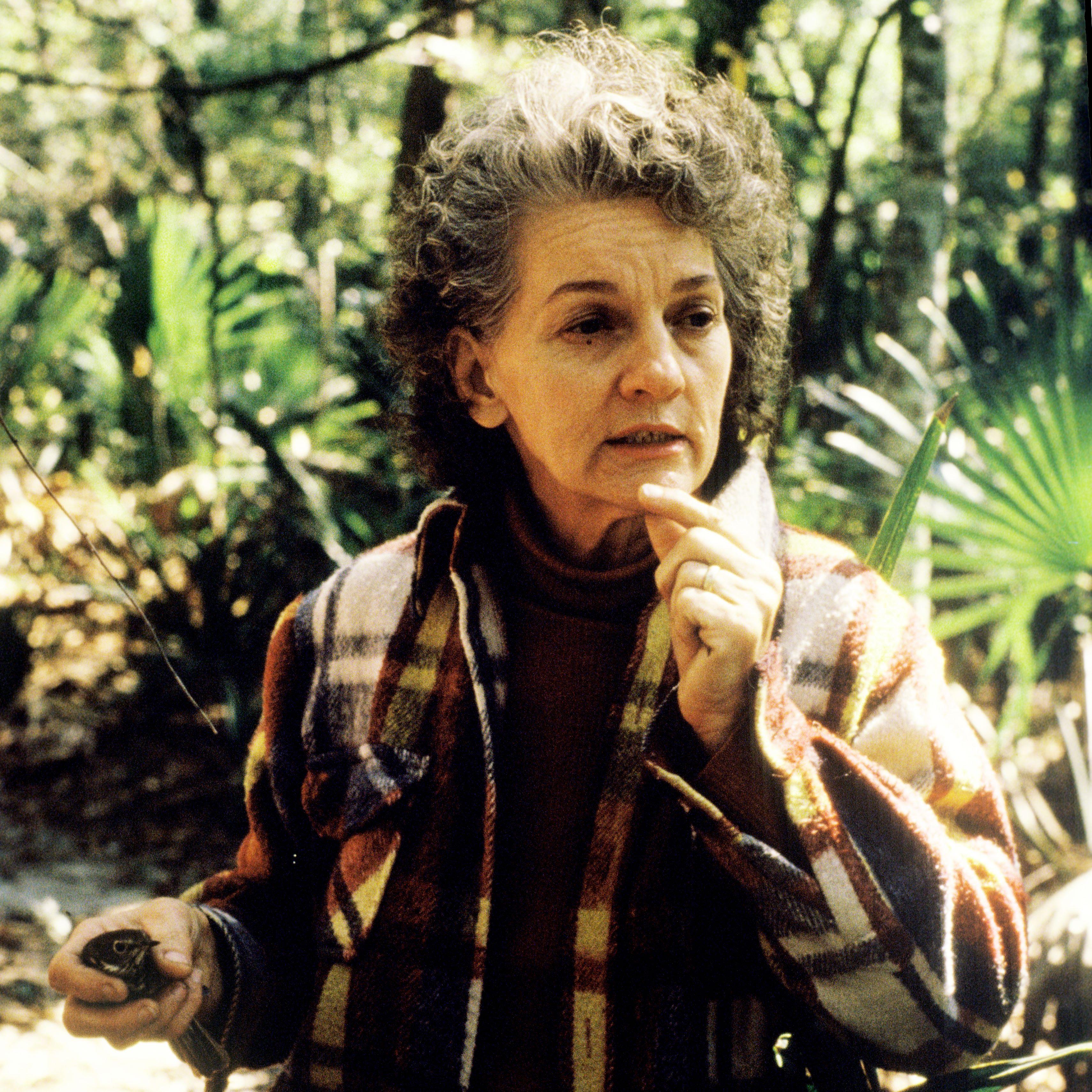 A woman holding a small bird in her right hand and gesturing with her left.