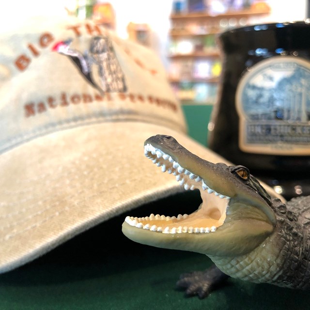 a toy alligator in front of a beige ball cap and black coffee mug