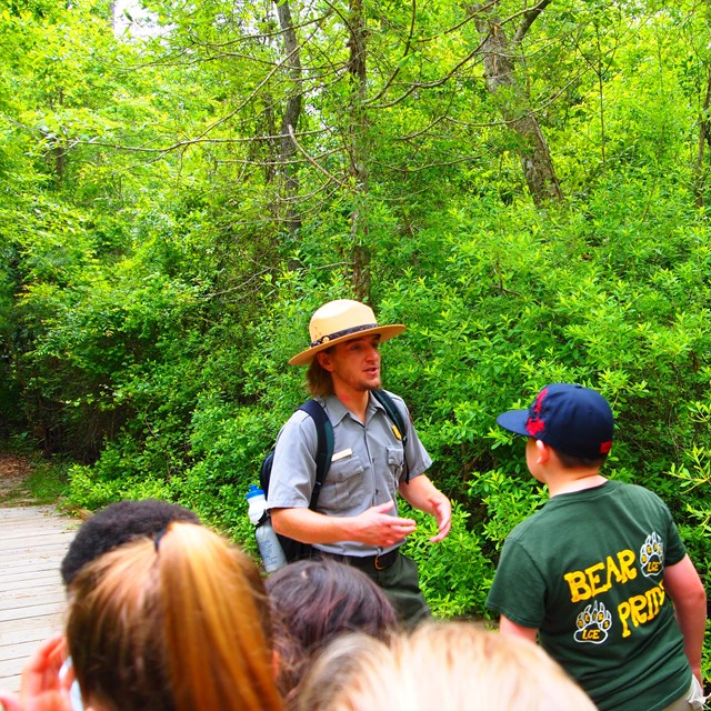 A ranger talking to a group of students in a forest.