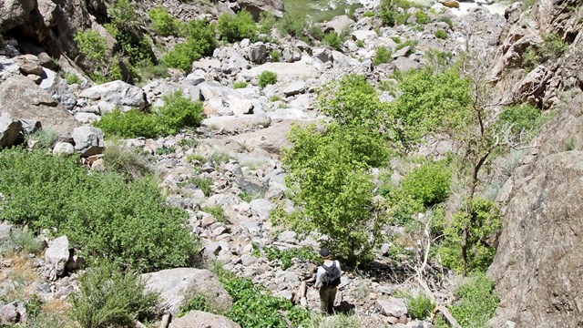 two hikers scrambling down rock ledges with the river below