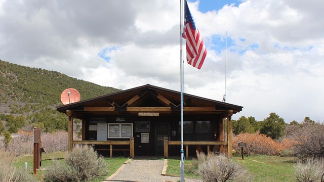 A wooden ranger station building with a porch. A flag, pole, and path are in front of the building