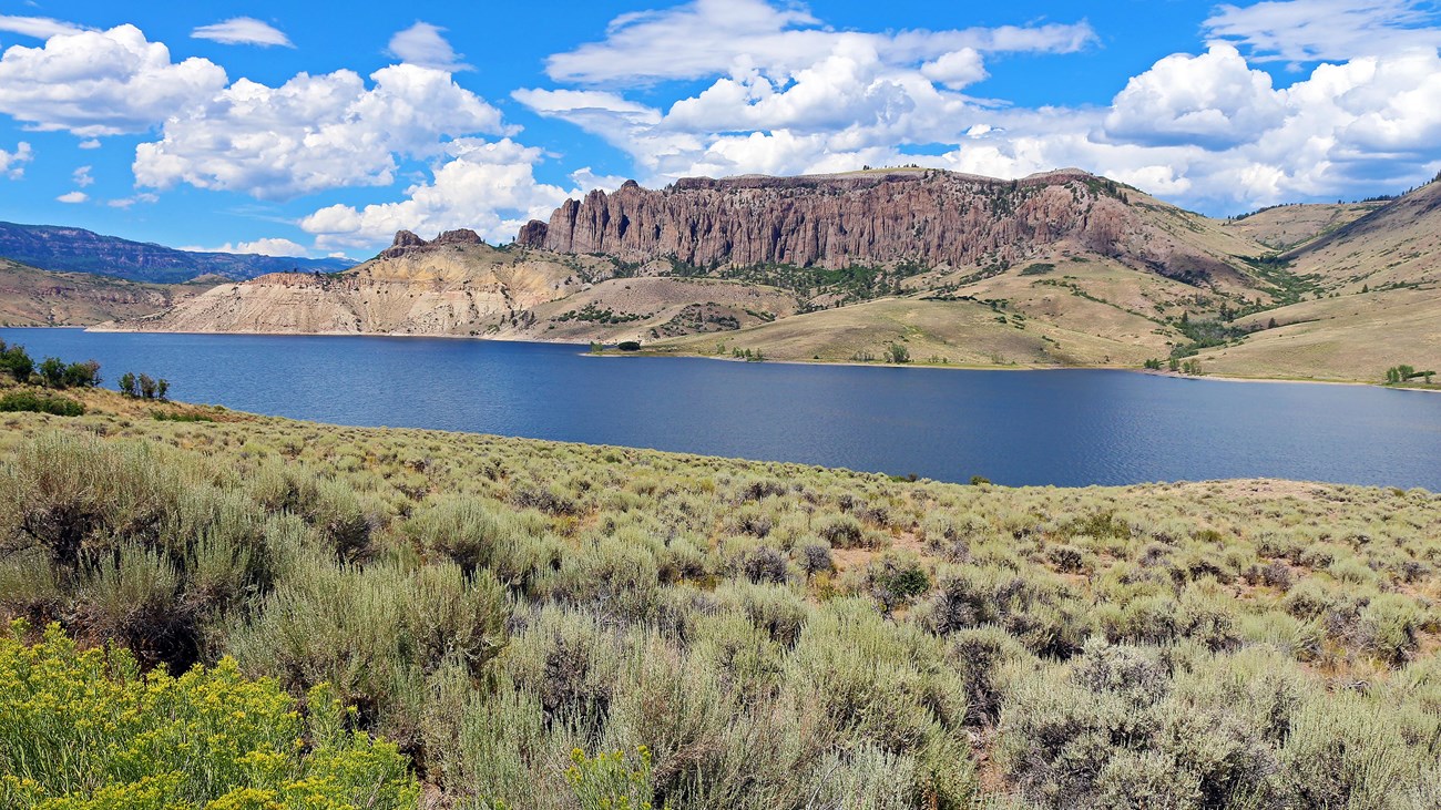 Distant rocky pinnacles rise above a large reservoir with sagebrush in the foreground.