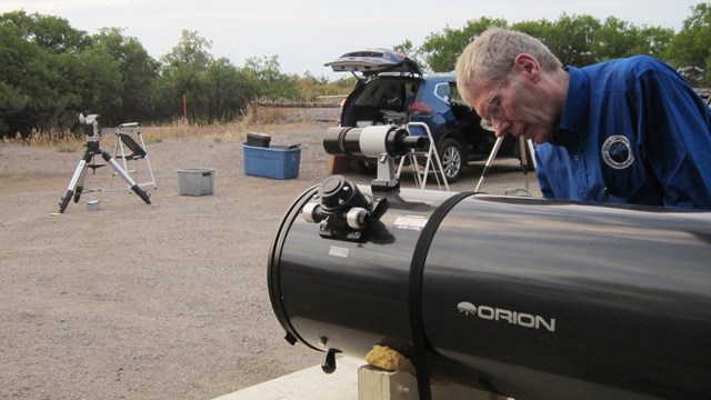 A person in a blue uniform standing by a telescope