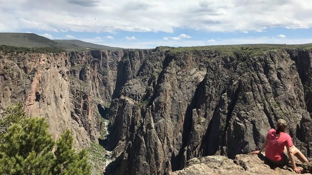 A hiker sits on a large rock overlooking Black Canyon.