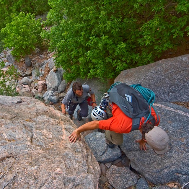 three hikers scrambling up steep rock ledges, viewed from above