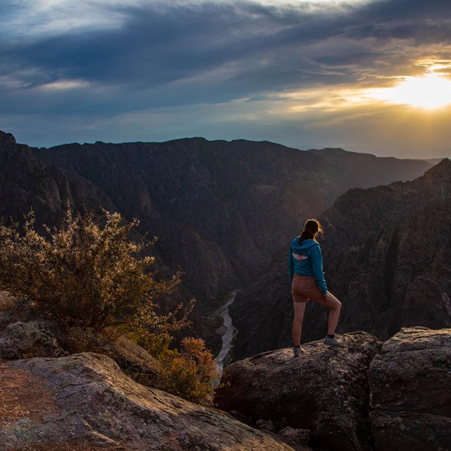 A person standing on a canyon edge looking at a sunset