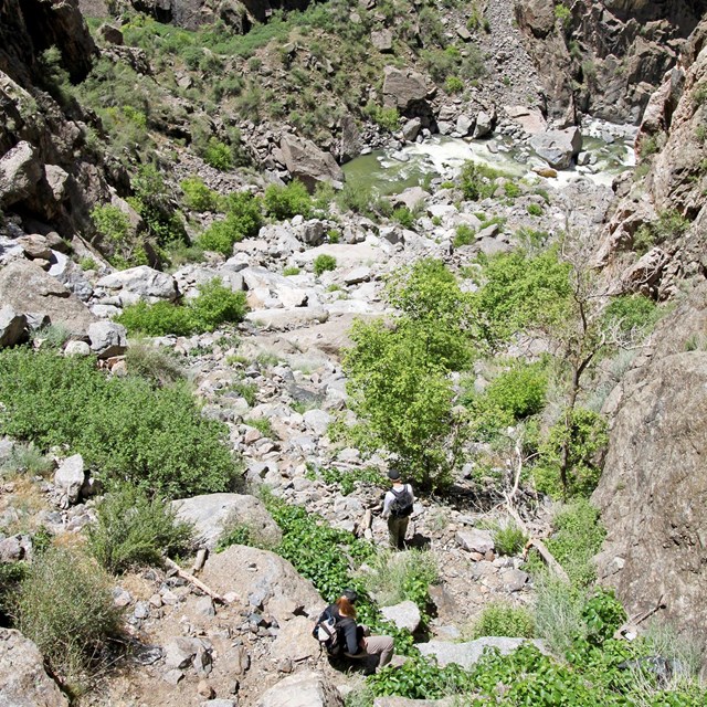 two hikers scrambling down rock ledges with the river below