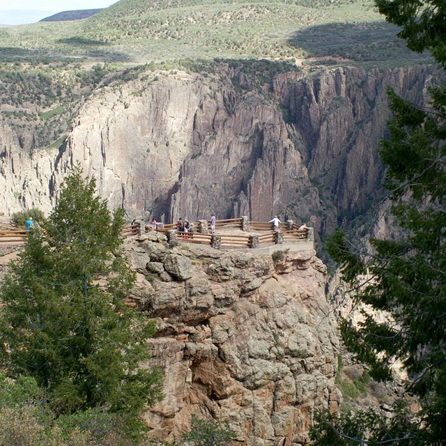 people standing at an overlook perched on a peninsula jutting into the Black Canyon