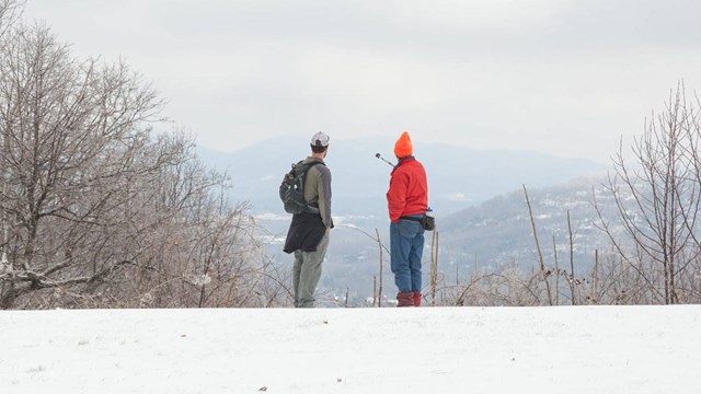 Two visitors looking out to mountainous view with snow covered ground.