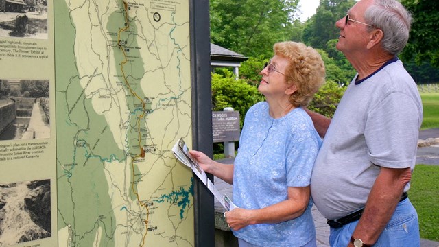 A man and women standing outdoors looking at an exhibit map