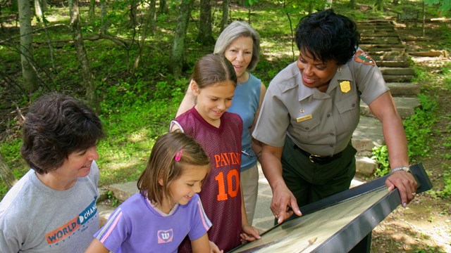 A ranger pointing out some information to four visitors on an outdoor exhibit panel