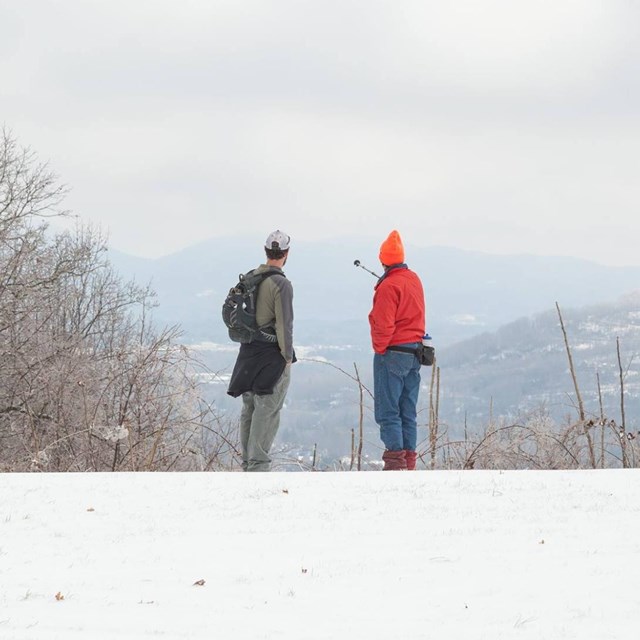 Two visitors looking out to mountainous view with snow covered ground.